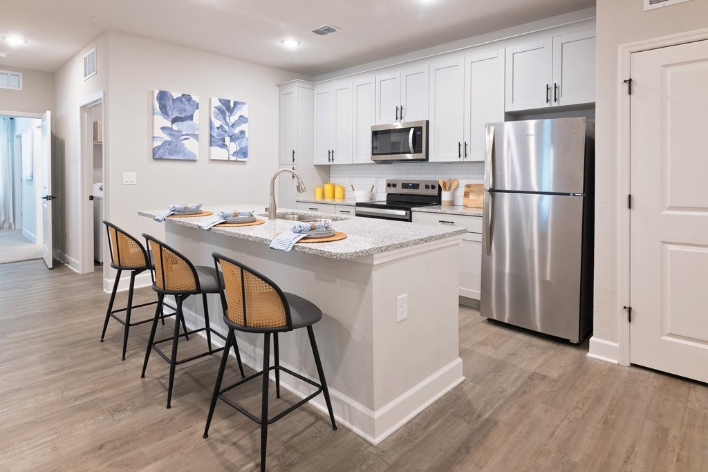 A kitchen with a refrigerator, sink, and bar stools.