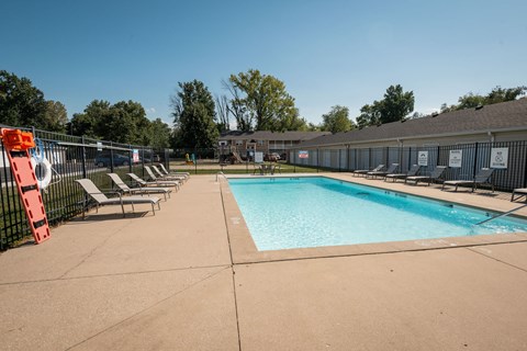 A large outdoor swimming pool surrounded by a fence and lounge chairs.