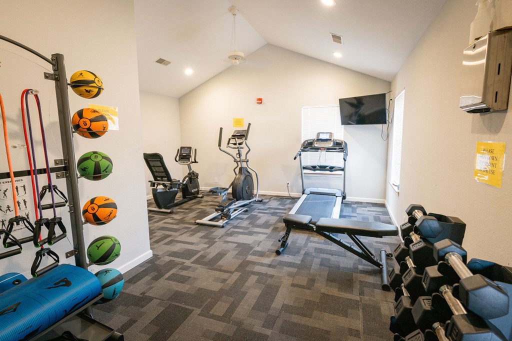 A gym with a variety of equipment including a treadmill, weights, and resistance bands.