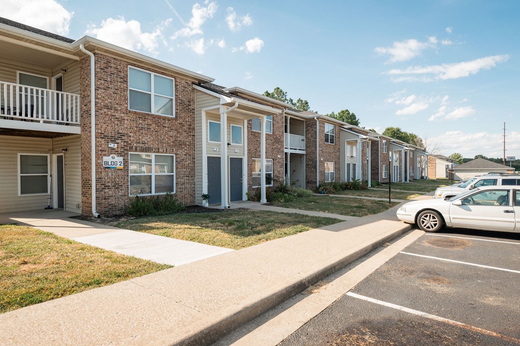 A white car is parked in a parking lot in front of apartment buildings.
