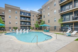 a swimming pool with lounge chairs and umbrellas in front of an apartment building