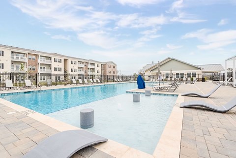 A large outdoor swimming pool with lounge chairs and a building in the background.