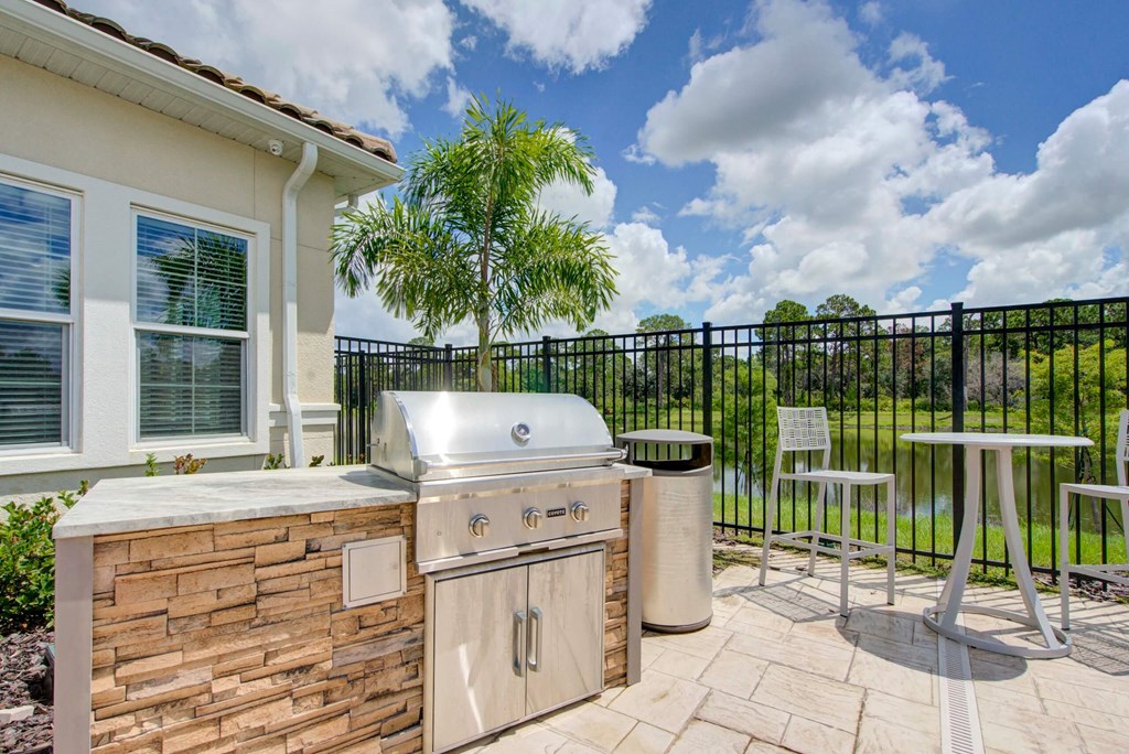 Grill and table with chairs and a pond in the background at flats at sundown luxury apartments in north port florida