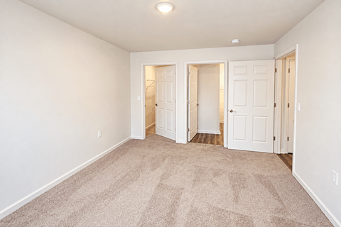 A room with carpeted floor and white walls with three doors.