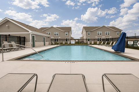 A swimming pool surrounded by lounge chairs in front of apartment buildings.