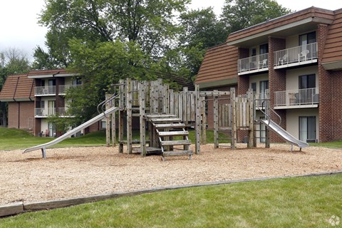 A playground with a slide and a wooden structure in front of apartment buildings.