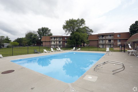 A swimming pool surrounded by a black fence and chairs.
