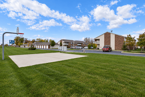 A basketball court is located in a grassy area in front of a building.