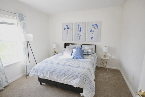 A bedroom with a bed, two lamps, and a painting on the wall.