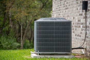 A large outdoor air conditioning unit sits on a concrete slab outside a brick building.