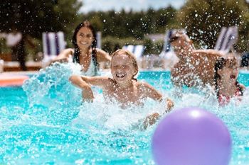 A group of people are playing in a pool with a purple ball.