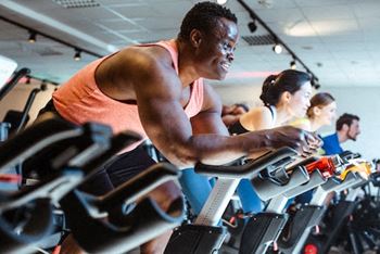A man in a pink tank top is working out on a stationary bike in a gym.