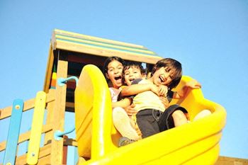Two children are playing on a yellow slide at a playground.