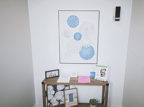 A table with a white and black floral tablecloth and a framed picture of blue and white flowers.