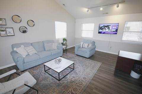 A living room with a grey couch, a white coffee table, and a television on the wall.