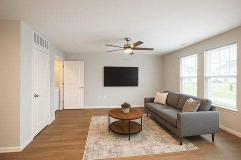A living room with a grey couch, a coffee table, and a flat screen TV mounted on the wall.
