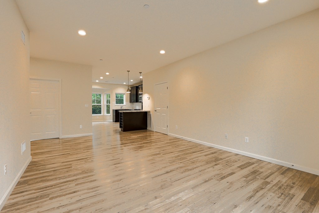an empty living room with wood flooring and a kitchen
