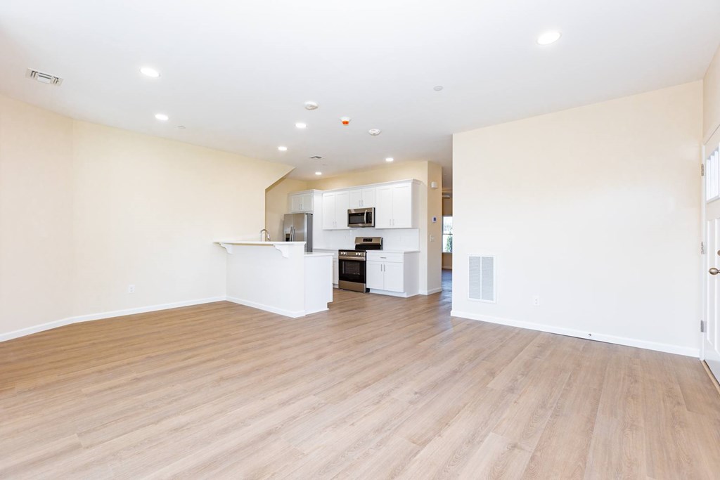 A spacious room with wooden flooring and a kitchen area in the background.