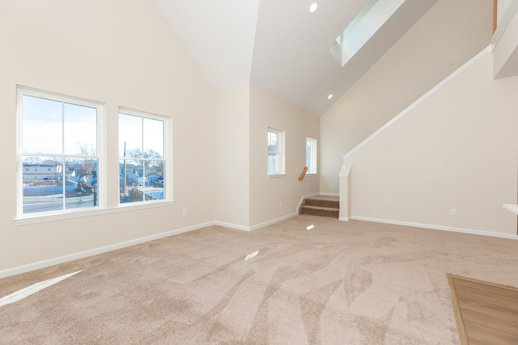 A large empty room with a carpeted floor and a staircase.