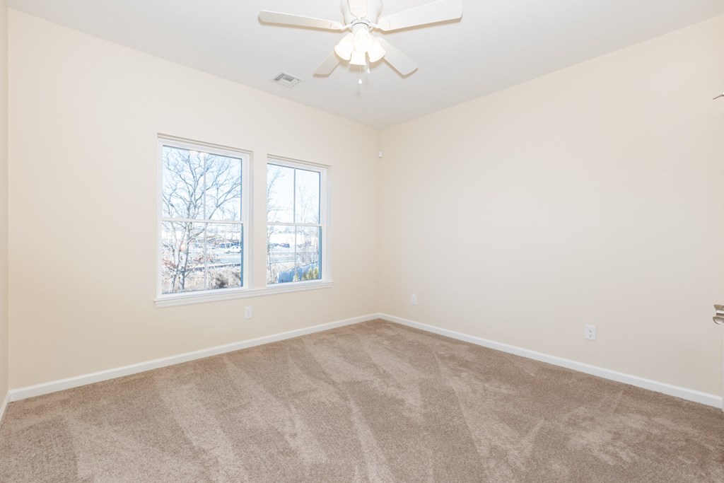 A room with a ceiling fan and two windows.