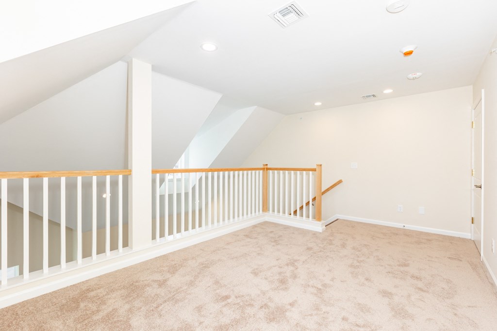 A spacious room with a carpeted floor and a staircase with a wooden railing.