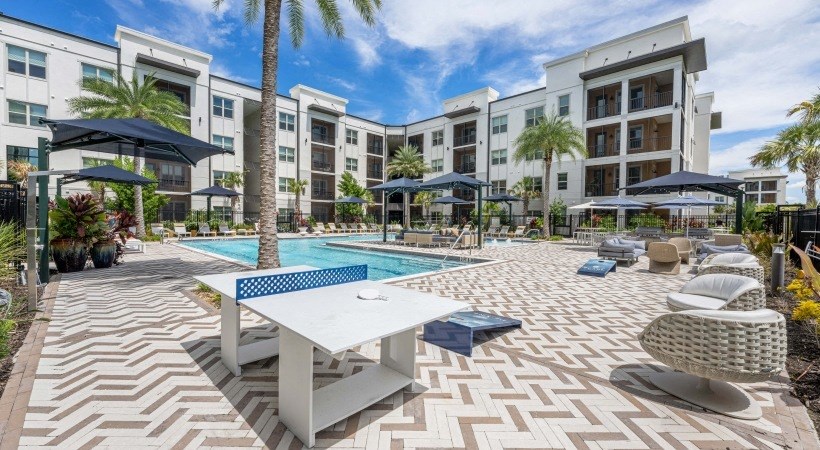 a swimming pool with a table and chairs in front of The Pearl apartments in Naples FL