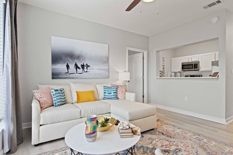 A living room with a white couch and a painting of three people walking on a beach.