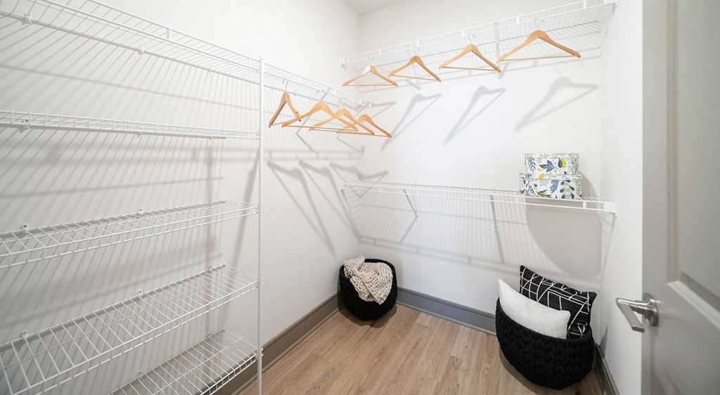 a walk in closet with white walls and shelves and a chair