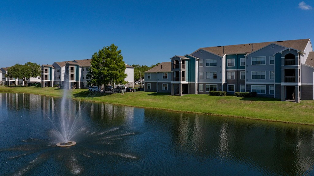 a fountain is in the middle of a pond in front of an apartment building