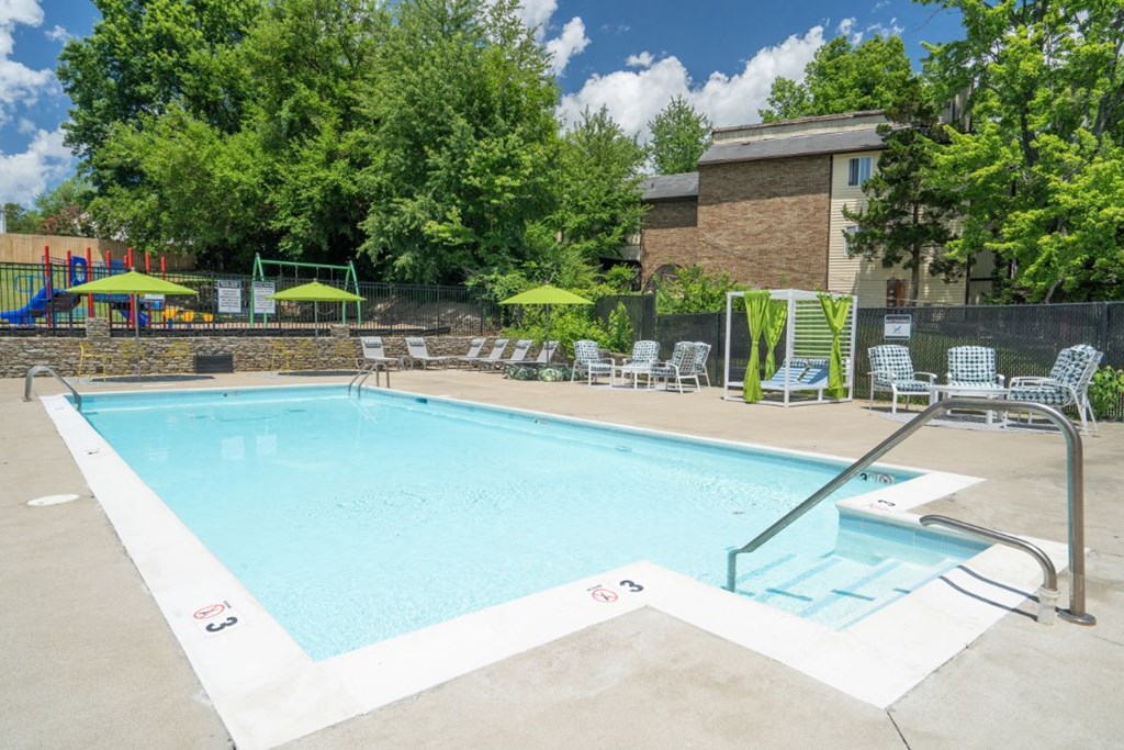 a swimming pool with lounge chairs and umbrellas in front of a brick building at Stonewater Apartments, Louisville Kentucky
