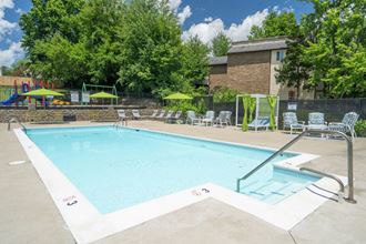a swimming pool with lounge chairs and umbrellas in front of a brick building at Stonewater Apartments, Louisville Kentucky - Photo Gallery 4