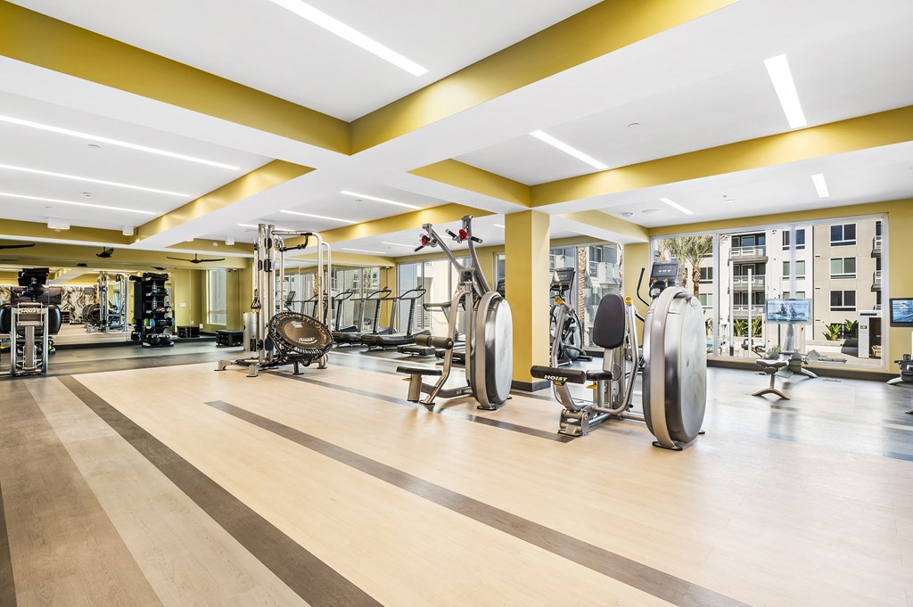 a gym with weights machines and a building in the background