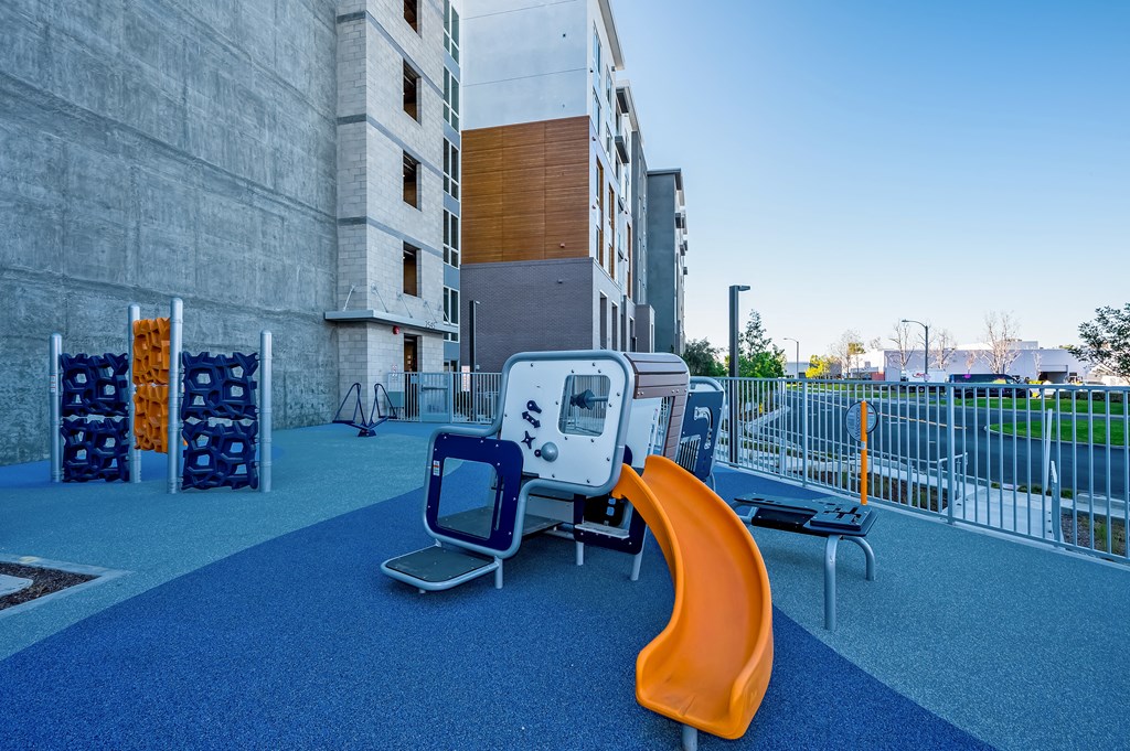 a playground with a slide and chairs in front of a building
