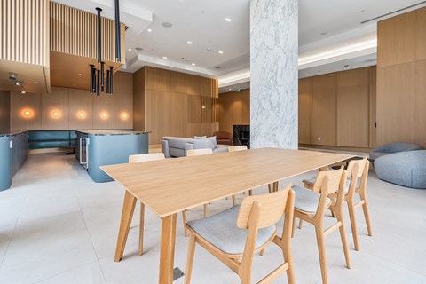 A long wooden table with chairs is in the middle of a room with a white marble pillar.