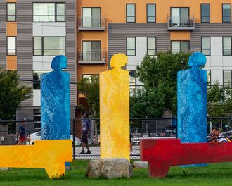 three sculptures in the grass in front of an apartment building