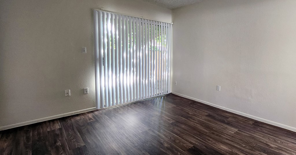 a bedroom with laminate wood floors, white walls, and a sliding glass door with long blinds
