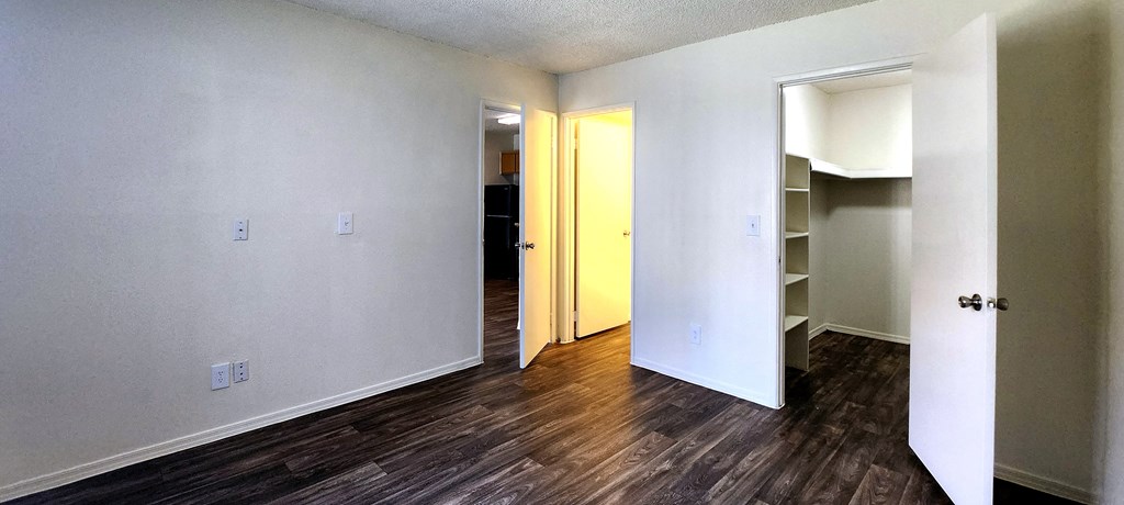 a bedroom with wood laminate floors, white walls and a walk in closet