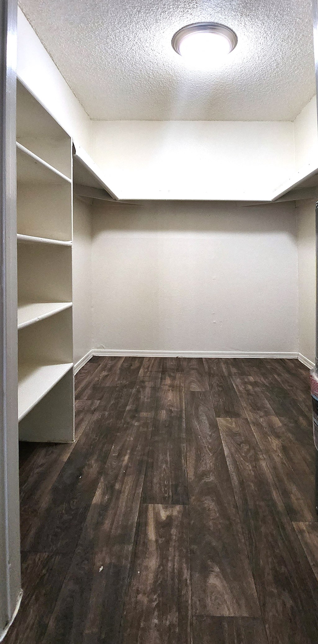 a walk in closet with wood laminet floor and white shelves
