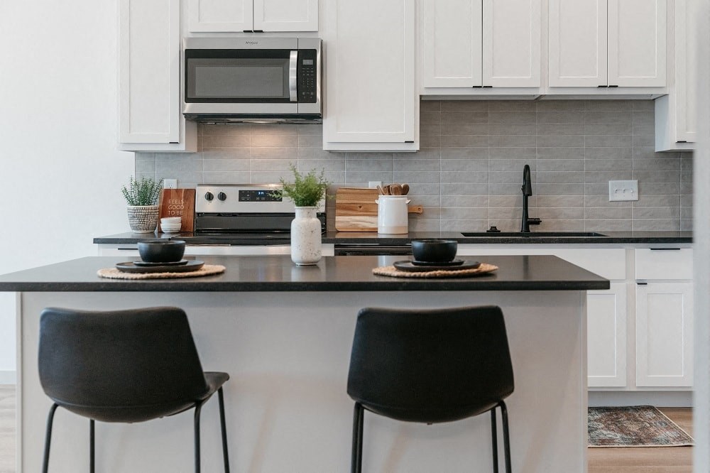 a kitchen with white cabinets and a counter with two black chairs