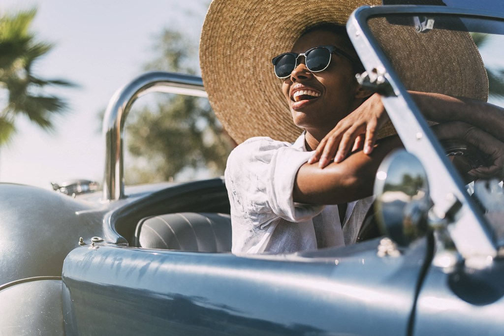 A person in a straw hat and sunglasses is driving a vintage car at Mayla Pompano, Pompano Beach, FL