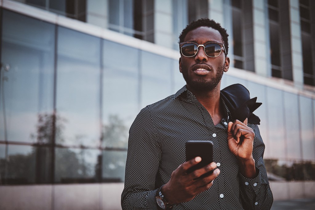 A man in a patterned shirt is holding a phone and adjusting his tie at Mayla Pompano, Pompano Beach, 33062