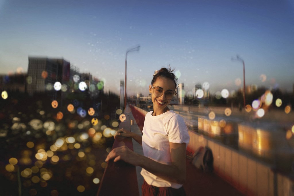 A woman in a white shirt and red skirt stands on a bridge with a cityscape in the background at Mayla Pompano, Pompano Beach, 33062