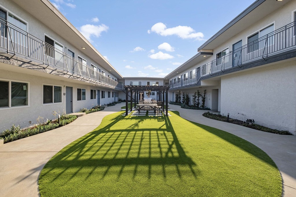 the courtyard of a building with a lawn and tables and chairs at Arlington Square Apartment , Torrance