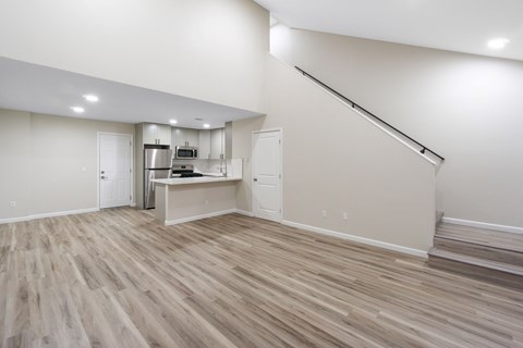 an empty living room with a kitchen area and a staircase