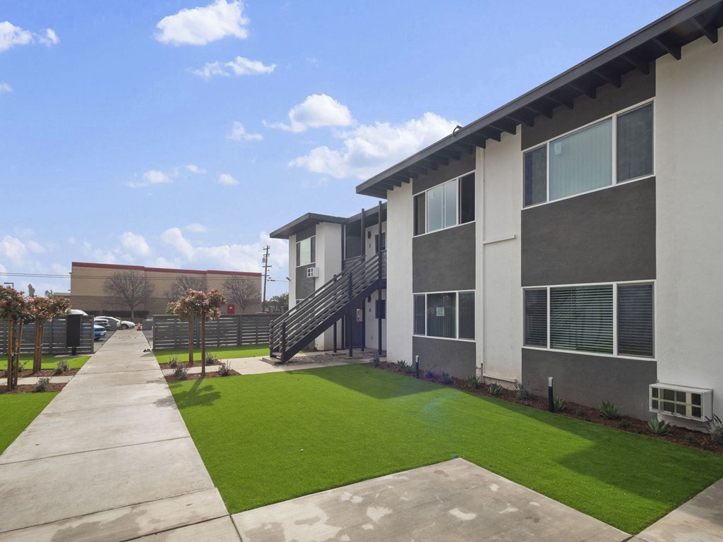 an exterior view of a building with green grass and a sidewalk at Charle Square Apartments, Costa Mesa, California