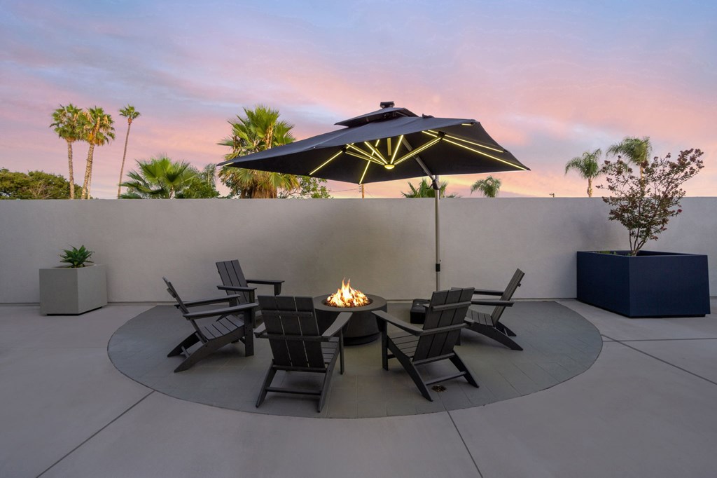 A patio with a fire pit and chairs under a black umbrella.at The Reserve La Mirada, La Mirada, California