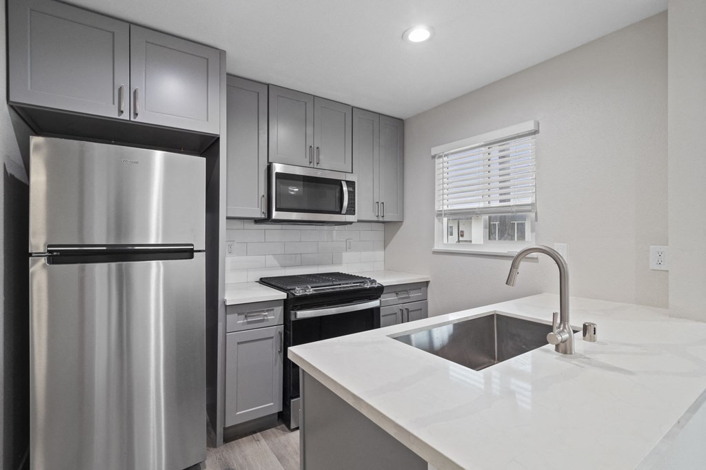 an empty kitchen with stainless steel appliances and white countertops at Charle Square Apartments, Costa Mesa