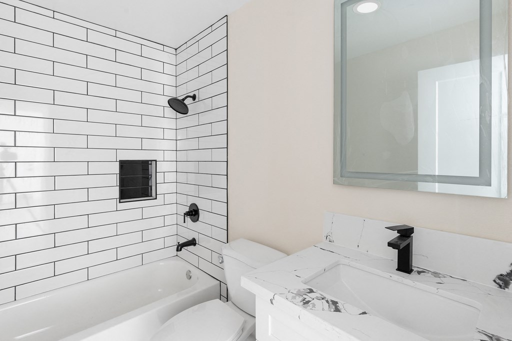 a white bathroom with white subway tile and black fixtures at Seaview Terrace Apartment Homes, California, 92672