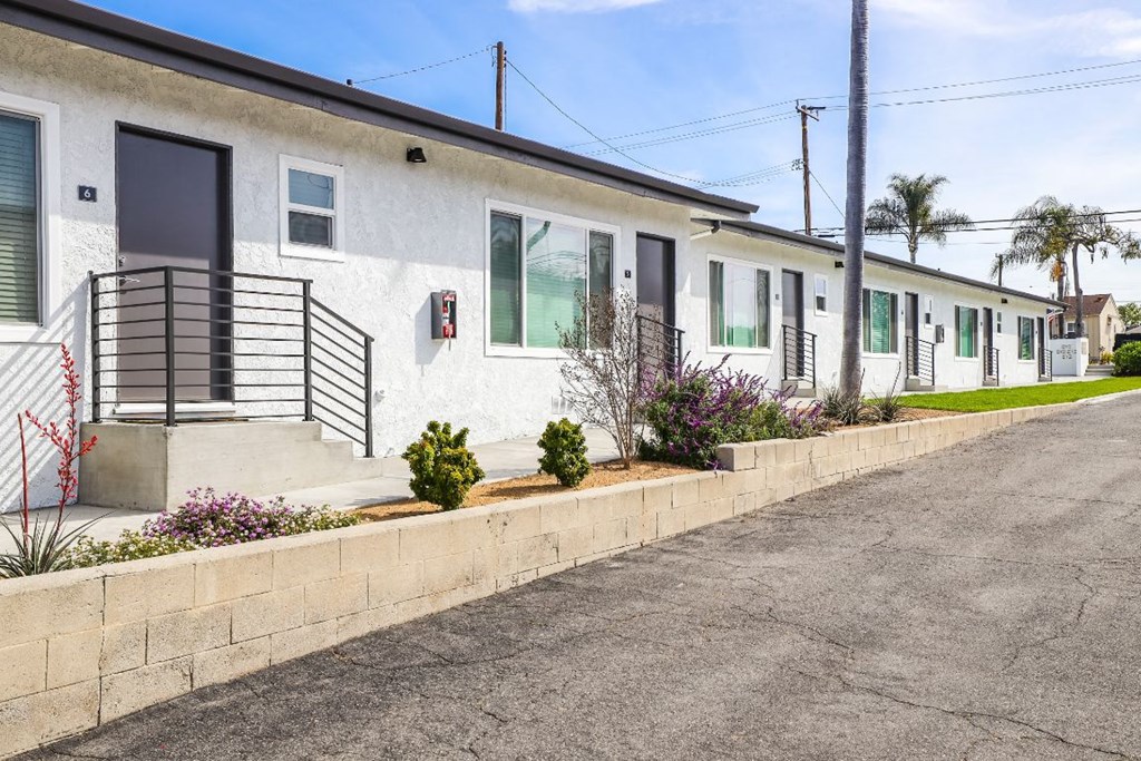 a row of white houses with green windows and a paved street