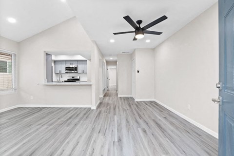 an empty living room with a ceiling fan and a kitchen
